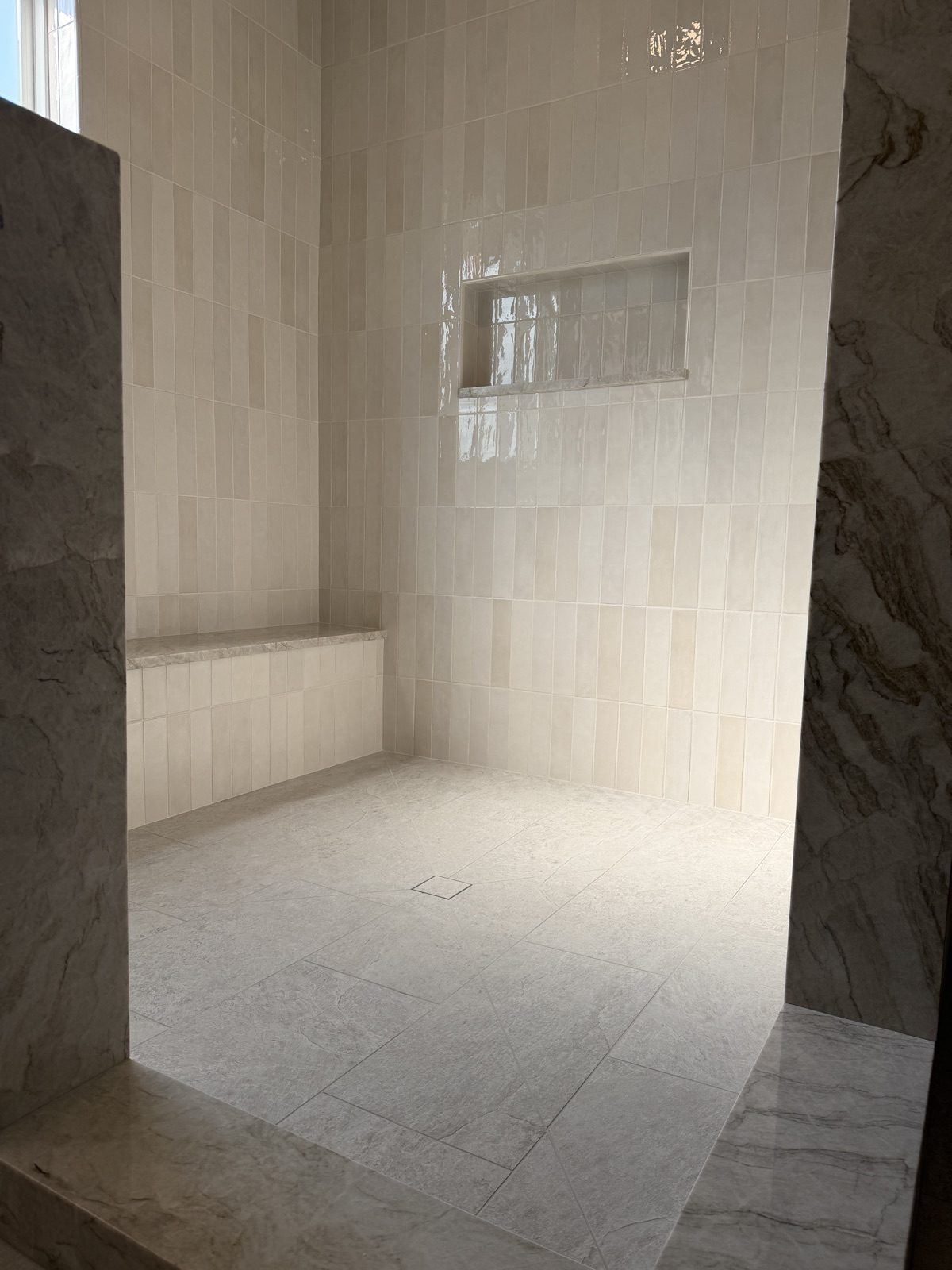 Ceramic subway tile stacked vertically in a shower with a stone bench, a niche shelf, and a fully wrapped curb, before the glass went in