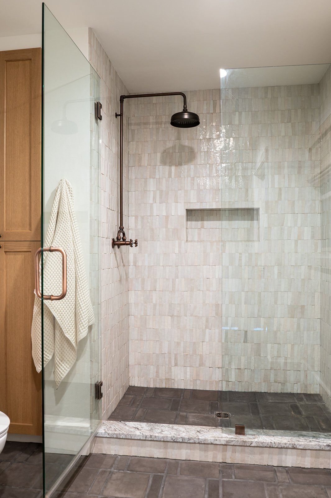Cream zellige shower: handmade glazed tile, a tiled niche, and copper fixtures